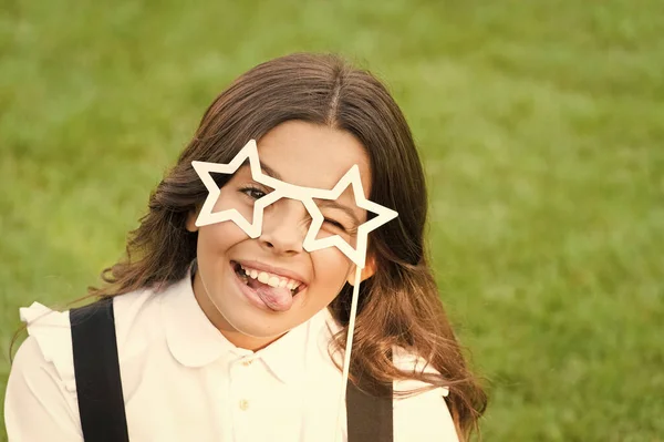 Engraçado criança feliz sair língua vestindo óculos em forma de estrela escola festa acessório para celebração na grama verde, dia das crianças — Fotografia de Stock