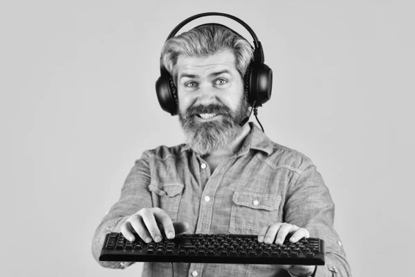 Jouer à des jeux informatiques. Plateforme de jeu en ligne. Jeux de loisirs modernes. L'arène du cybersport. Guide de construction de PC de jeu. Paramètres graphiques. Dépendance au jeu. Homme barbu hipster gamer écouteurs et clavier — Photo