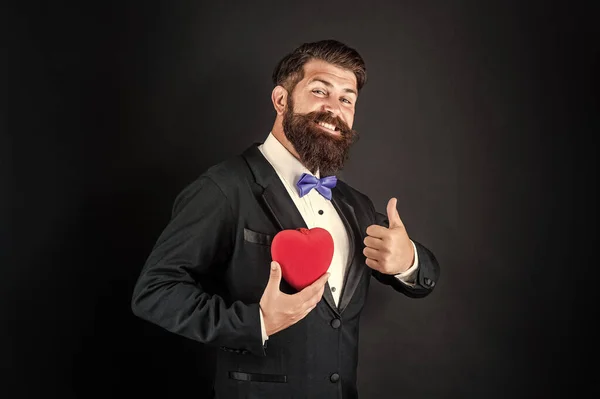 Feliz smoking homem com barba segurar romântico amor coração mostrar polegar para cima, feliz dia dos namorados — Fotografia de Stock