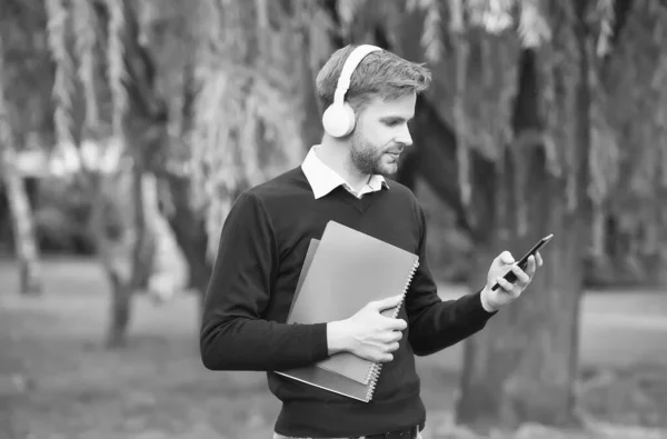 Unshaven guy holding notebook and listening music in earphones from smartphone, education — Stock Photo, Image