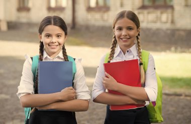 Ders çalışırken iyi eğlenceler. Okul üniformalı mutlu kızlar. Sırt çantalı gülümseyen genç öğrenciler. İlkokulda eğitim. Öğrenci kızlar birlikte ders alıyorlar.