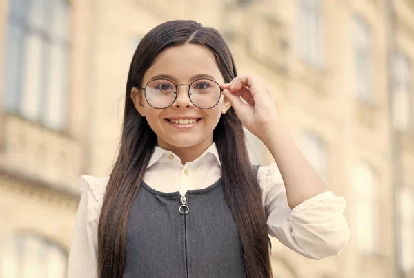 학교에서 교복을 입은 행복 한 소녀는 밖에 있는, 전문가들 이 또렷하게 볼 수있도록 패션 액자에 안경을 고정 시킨다 — 스톡 사진