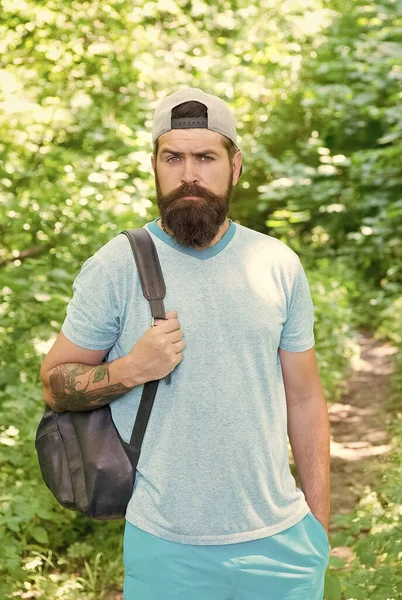 De pie solo en el bosque al aire libre con la naturaleza puesta del sol en el fondo. Hombre barbudo con mochila. retrato de moda del hombre barbudo. chico maduro en sombrero. viajero hipster serio — Foto de Stock