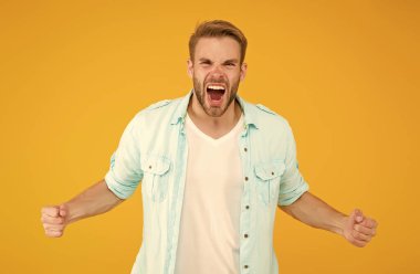 saf öfke. negatif insani duygular. Havalı saç stili olan seksi çocuk tişört giyiyor. Tıraşsız, tüylü yakışıklı bir adam. Erkek yaz modası. Öfkeli adam saçını tarayıp bağırıyor.