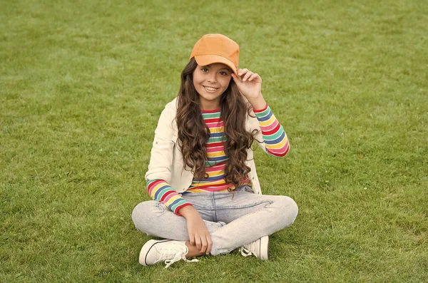 Vrije tijd. mode voor kinderen. Zonnige lentedag. Vrolijk schoolmeisje ontspannen op groen gras. glimlachende pupil kind dragen casual stijl. terug naar school. Gelukkige kinderdag. klein meisje outdoor — Stockfoto