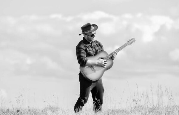 Play beautiful melody. Country music concept. Guitarist country singer stand in field sky background. Inspired country musician. Hiking song. Handsome man with guitar. Country style. Summer vacation