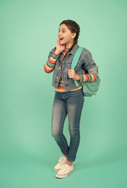 Sıradan moda tarzındaki meraklı kız çantasıyla mavi arka planı ve merakı olan bir seyahat çantası taşıyor.