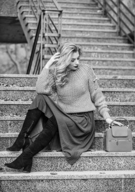 Sonbahar moda trendi. Giyilebilir trendler. Kız eteğinin üstüne daha büyük bir katman örülmüş. Sonbahar formülü. Sonbahar için stil süveter ve etek karışımı. Muhteşem kadın saç stili merdivenlerde oturuyor. Sıcak sonbahar