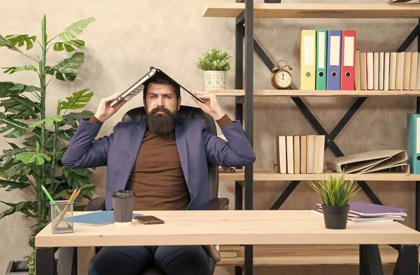 Seriózní podnikatel ve formálním stylu držet notebook na hlavě sedí v moderní kanceláři, e-business — Stock fotografie