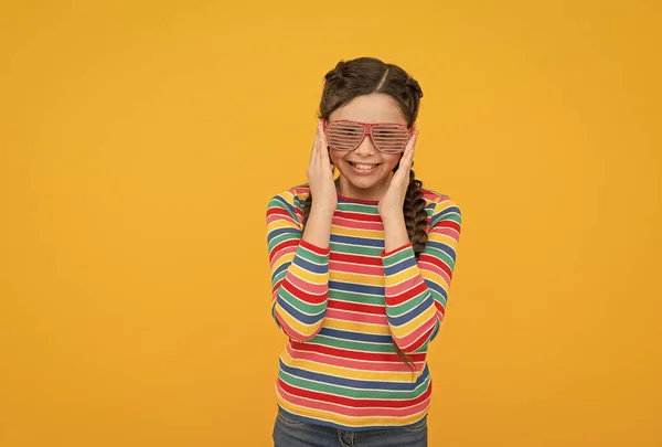 Niña feliz con pelo trenzado desgaste color arco iris y glamour partido gafas sobre fondo amarillo, tiempo de diversión —  Fotos de Stock