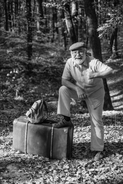 Resor är min terapi. Glad pensionär visar tummen upp i naturen. Njuter av att resa. Gamling med retro resväska utomhus. Resa och resa. Sommarsemester. Vandringslust. Säg ja till att resa — Stockfoto