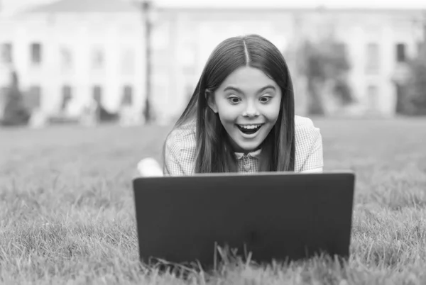 Здивована дівчина-підліток розслабляється в парку на зеленій траві на шкільному подвір'ї, концепція комп'ютерної залежності — стокове фото