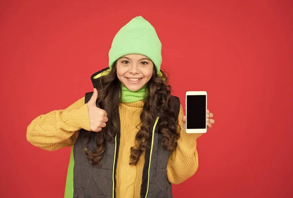 Menina criança extremamente feliz com cabelos longos usar roupas quentes e apresentando telefone móvel moderno, melhor oferta — Fotografia de Stock