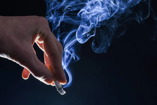 Male hand hold cigarette butt with smoke swirls dark background, nicotine addiction — 图库照片