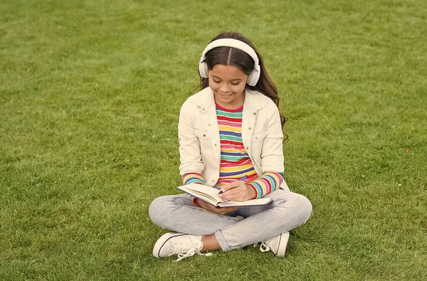 在线学习。教育播客。让它成为现实。在室外听音乐。小女孩喜欢音乐，坐在草地上。快乐的时光。儿童耳机听音乐。很酷的女孩耳机听音乐 — 图库照片
