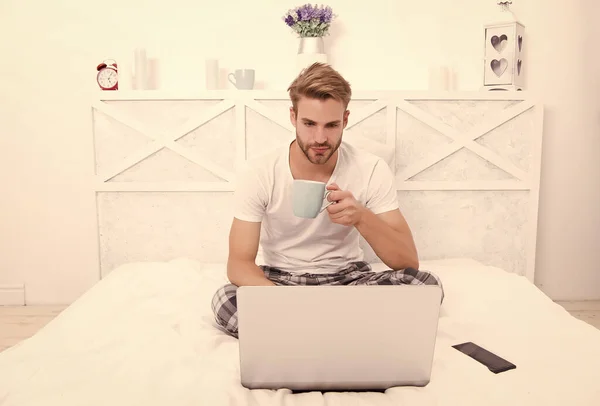 Kaffe för eftertanke. Seriös man dricker kaffe med laptop i sängen. Morgonrutin. Varm kopp — Stockfoto