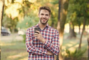 Gülümseyen traşsız adam sabah kahvesini dışarıda kareli gömlekle içiyor, ilham veriyor.