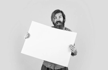 Sakallı, şık saçlı, beyaz tenli hippi. Elinde fotokopi alanı olan kağıt pankart var.