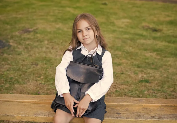 Söt liten barn med allvarligt utseende i formell uniform hålla skolväska sitter på parkbänk, skolan beredskap — Stockfoto