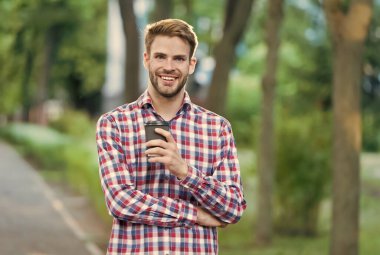 Sokakta elinde kahve fincanı olan mutlu bir adam kareli gömlek, içki ve insanlar giyer.