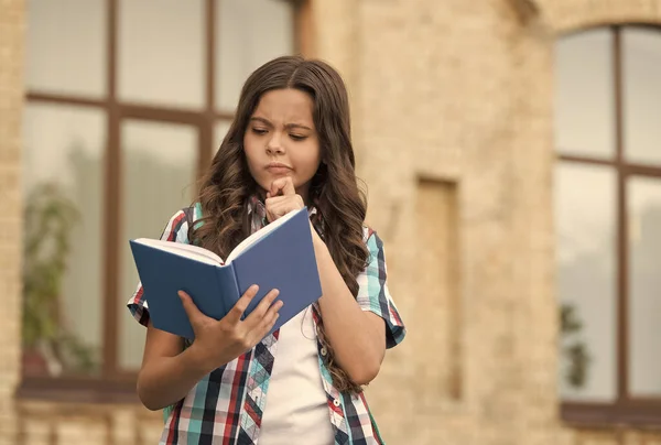 Plus vous lisez, plus vous apprenez. Un enfant sérieux lit un livre à l'extérieur. Bibliothèque scolaire. Éducation à l'alphabétisation. Cours de lecture. Lecture à domicile. Littérature et langue. Fantaisie et imagination — Photo