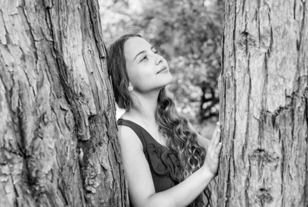 Little kid dreamer with long wavy hair and beauty look dream at tree trunk in summer park, future. Black and white.