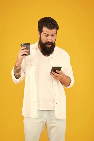 Sorprendido chico con bigote y barba beber café y ver noticias en el teléfono inteligente, repentinidad — Foto de Stock