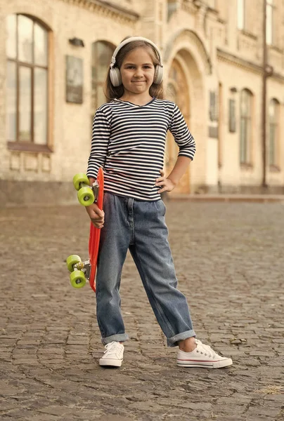 Bambina tenere penny board ascoltare musica in cuffie moderne estate all'aperto, vagabondaggio — Foto Stock