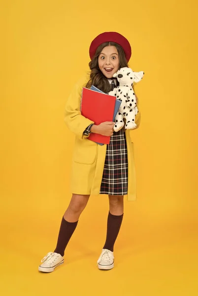 教育概念。童年的快乐学校和时尚。穿着学生服的孩子。穿着法式贝雷帽，背景是黄色的。时尚的青少年大学生。带着玩具狗和笔记本的小女孩 — 图库照片