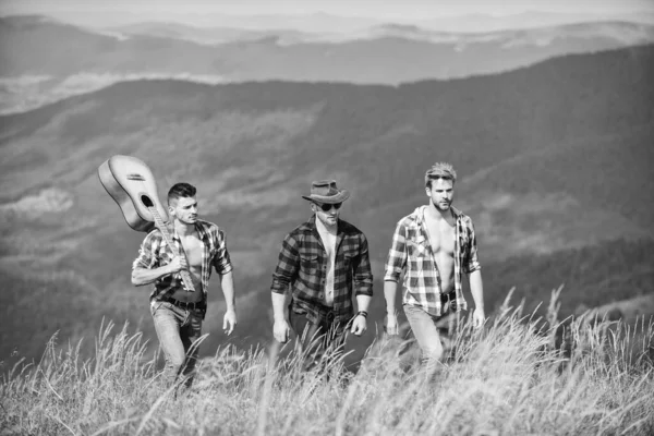 Lång väg. Ungdomar i rutiga skjortor går tillsammans på toppen av berget. Män med gitarrvandring på solig dag. Turister vandring koncept. Vandring med vänner. Njuta av friheten tillsammans — Stockfoto