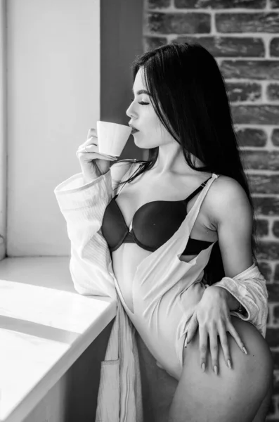 Kaffe på morgonen ger henne humöret. Sensuell tjej njuter av sitt aromatiska morgonkaffe. Sexig kvinna dricker hälsosam morgondryck vid fönstret. Kaffe väcker henne på morgonen — Stockfoto