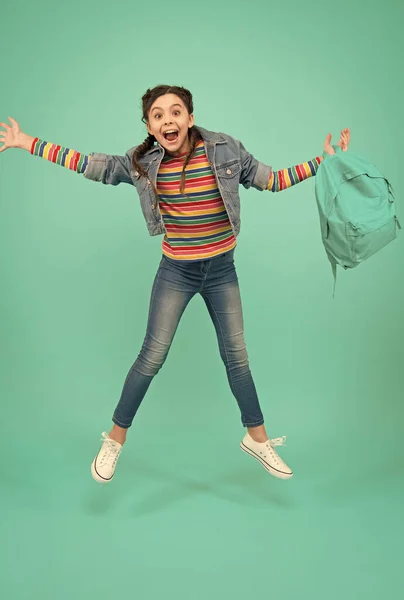 Joyeux saut énergique enfant avec sac d'école dans un style décontracté fond bleu, enfance — Photo