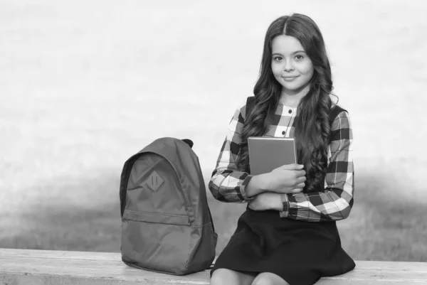 Klein kind in formeel uniform ruim boek zitten op park bank met schooltas, kennis — Stockfoto