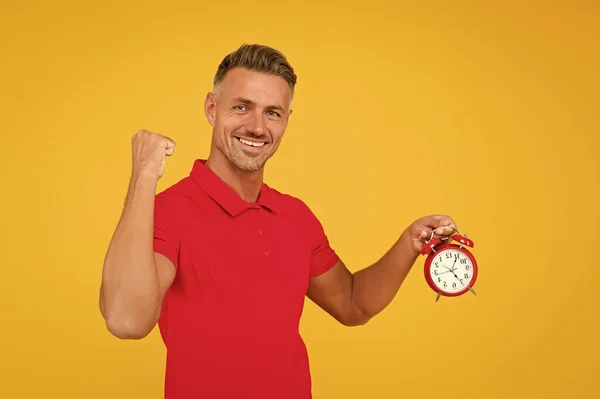 Feliz caucásico chico flex fuerte brazo celebración alarma reloj amarillo fondo, puntualidad — Foto de Stock