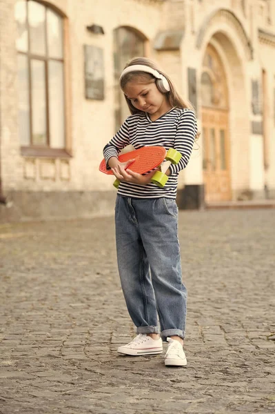 Bambino piccolo tenere penny board e ascoltare musica in cuffie all'aperto, skateboard — Foto Stock