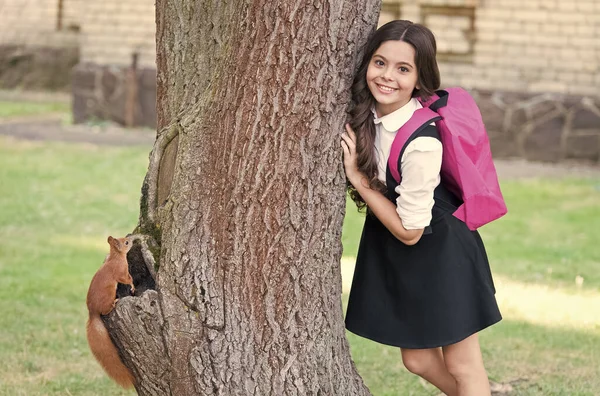 Boldog kis gyerek egyenruhában iskolatáskával hátizsákkal mókus mászás fa a parkban, zoológia. — Stock Fotó