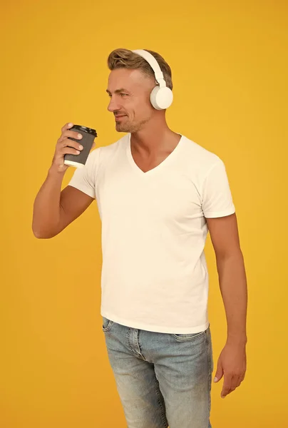 Boldog jóképű férfi zenét hallgat fülhallgatóban elvitelre való kávéscsészét iszik, szünetet tart. — Stock Fotó