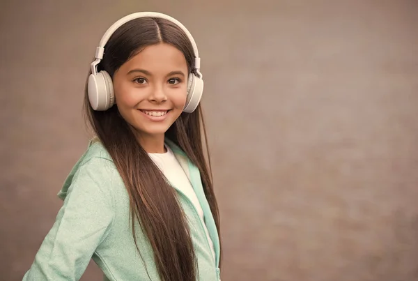 Felice ragazza della scuola ascoltare musica o audiolibro in cuffie per l'istruzione e la gioia, nuova tecnologia, spazio copia — Foto Stock