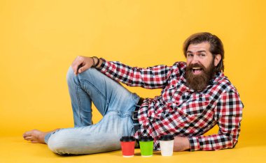 Kareli gömlekli, modaya uygun saç stili olan beyaz, olgun bir hippi sabah kahvesini kağıt bardaktan, kahveden seçer.