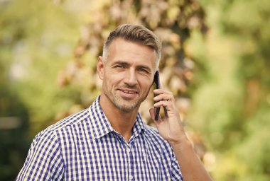 Erkek, dışarıda cep telefonundan konuşuyor. Yakışıklı adam hareket halinde. Erkek muhabbet eder. Modern hayatta iletişim. Çevik iş. Olgun traşsız erkek gömleği