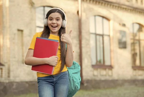 Utbildning för barn. Lyssna på musik. Lycklig barndom. En liten flicka bär hörlurar. Modern teknik inom utbildning. Glada flicka hålla mapp. Tillbaka till skolan. lycklig unge med anteckningsbok — Stockfoto