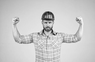 İnşaat kaskı ve kareli gömlek giyen yakışıklı adam inşaat alanında güç gösterisi yapıyor, erkek gücü.