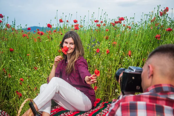 Ζευγάρι στην αγάπη του άνδρα και της γυναίκας λήψη φωτογραφιών στην κάμερα στο καλοκαιρινό χωράφι με τα λουλούδια παπαρούνας, φωτογράφος — Φωτογραφία Αρχείου