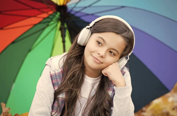 Szczęśliwy dzieciak nosi słuchawki pod kolorowym parasolem. Dziewczyna słucha muzyki. dziecko zrelaksować się w jesiennym lesie. Jesienne liście w parku. Z powrotem do szkoły. edukacja online. sezonowa deszczowa pogoda — Zdjęcie stockowe