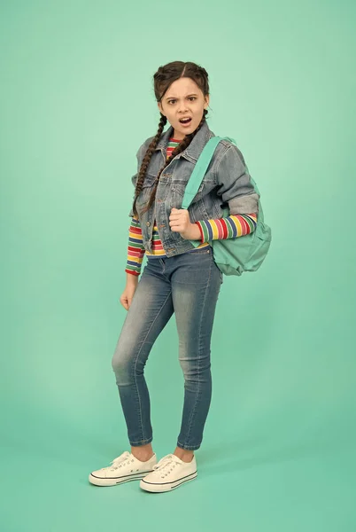 Criança infeliz com olhar irritado no estilo de moda casual levar mochila fundo azul, escola — Fotografia de Stock