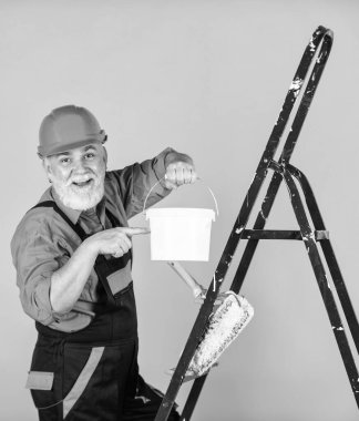 Boyalı kovayla şapkalı bir ressam. İnşaat işçisi boyama cephesi. Isı yalıtımı işe yarıyor. Boyacı merdiveni. Onarım yapmak için. İş elbiseli bir adam boş odada duvar boyuyor.
