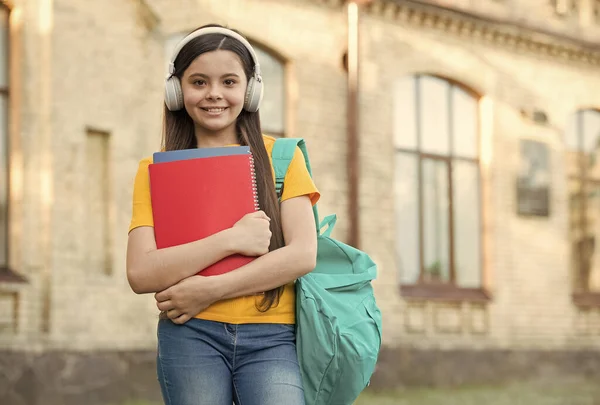 Schoolonderwijs in het moderne leven. terug naar school. Tiener meisje luisteren audio boek. kind met notitieboekje op school. Gelukkig kind met map. klein meisje dragen oortjes buiten — Stockfoto