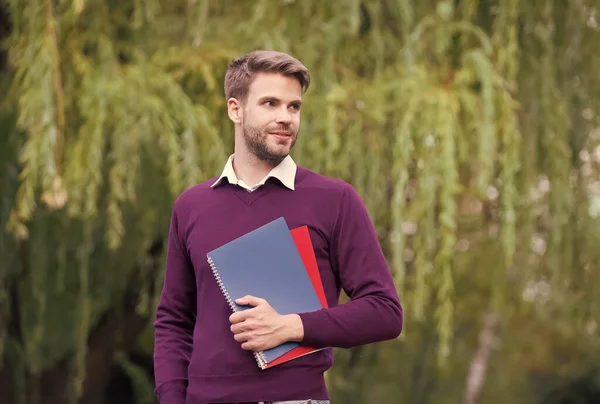 Bel homme non rasé avec un classeur dans ses mains regardant dans la distance en plein air, journée de la connaissance — Photo