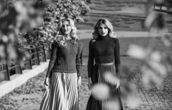 Fall fashion. Pleated skirt fashion trend. Women walking in autumn park. Friends girls. Autumn stylish outfit. Adorable ladies enjoy sunny autumn day. Fashionable clothes. Femininity and tenderness