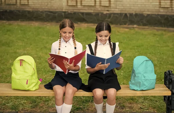 Crianças em uniformes escolares lêem livros de biblioteca sentados no banco ao ar livre, lendo — Fotografia de Stock